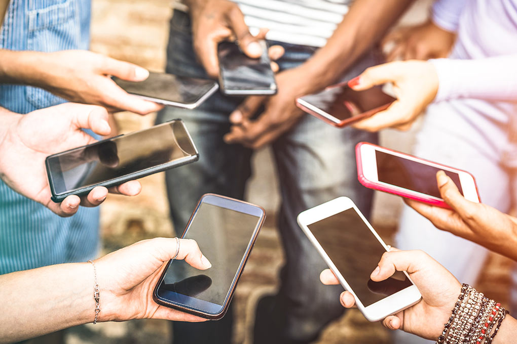 A group of different people holding different cell phones to text in SMS keywords.