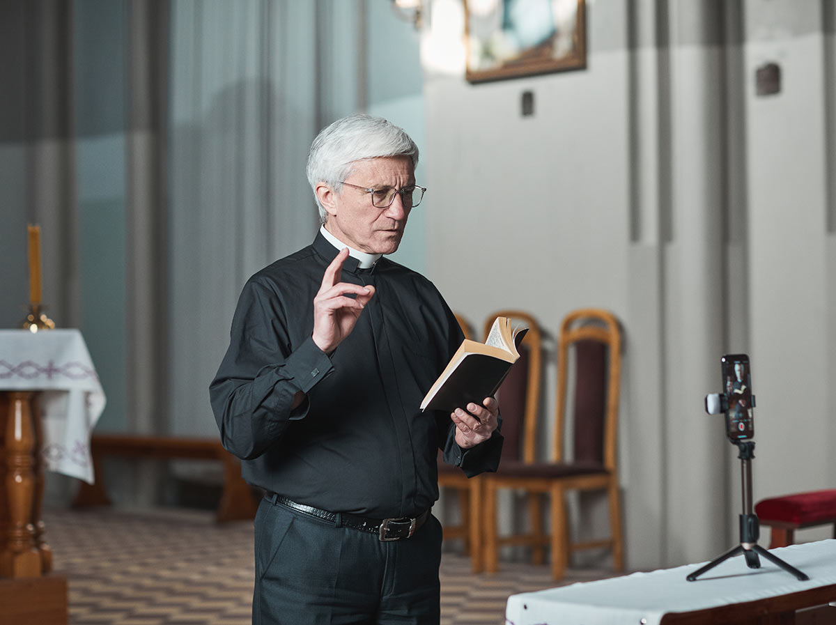 A priest records a sermon on his phone to send to congregation members.