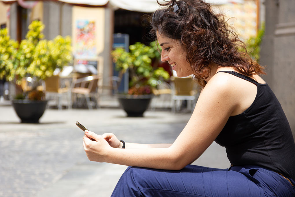 A smiling woman sends a text message on the church steps.